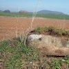 Močidlec - Mikuttův kříž | poškozený kamenný sokl Mikuttova kříže na okraji pole u Močidlece částečně zahrnutý zeminou - duben 2016